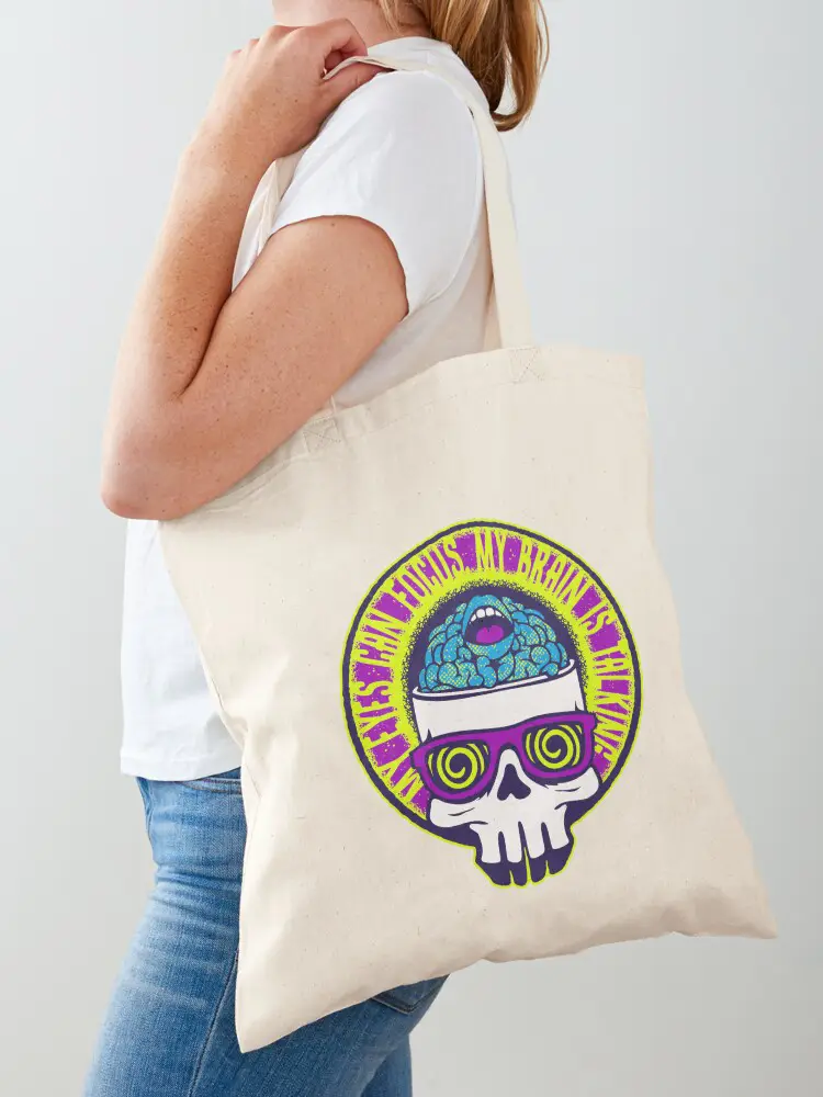 A person carrying a cream-colored canvas tote bag featuring a large psychedelic skull illustration, blending urban fashion with functional, eco-friendly accessories.