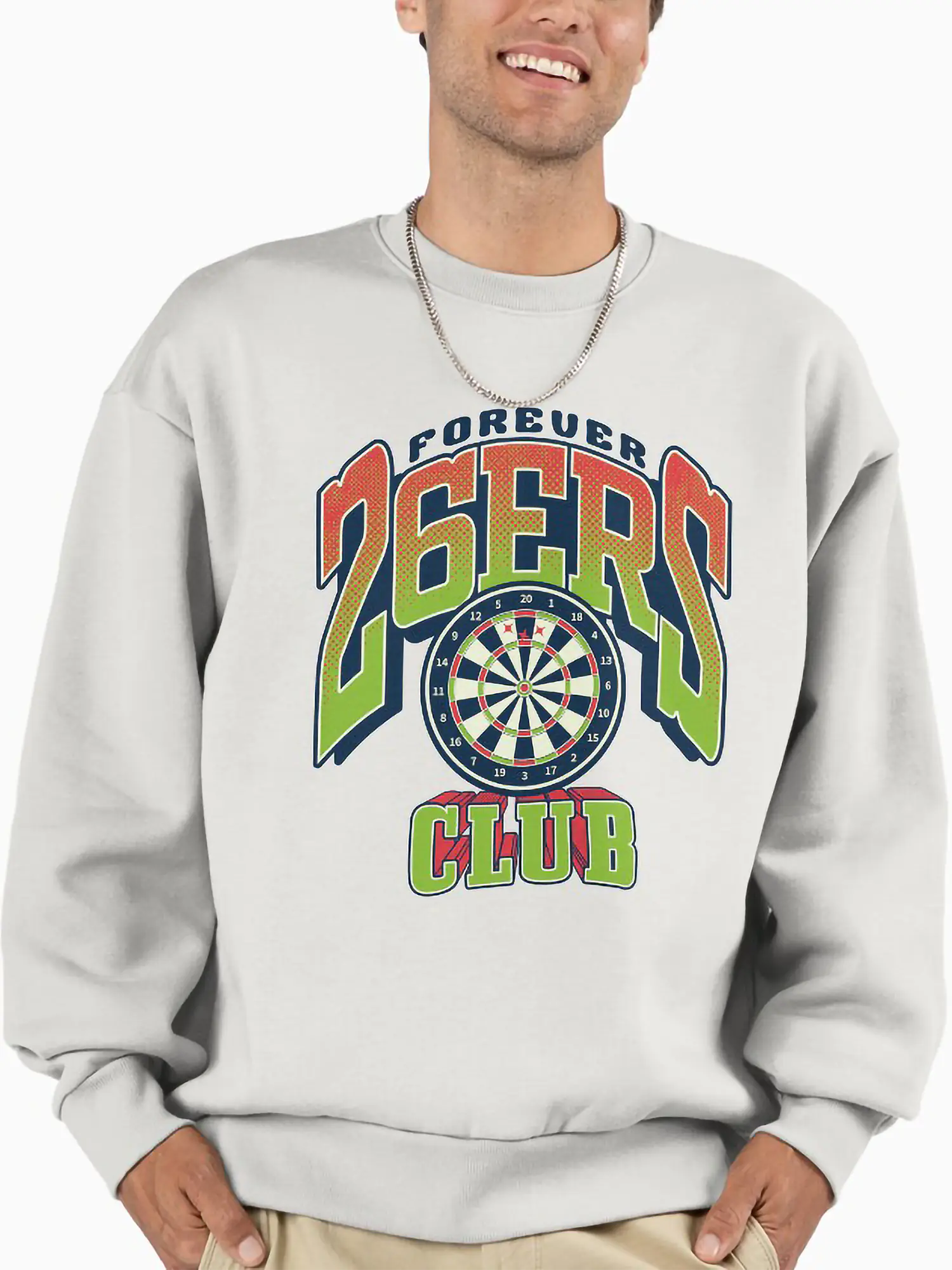 A man with a friendly smile wearing a light grey crewneck sweatshirt featuring the "FOREVER 26ERS CLUB" logo with an orange and green gradient dartboard graphic on the chest.