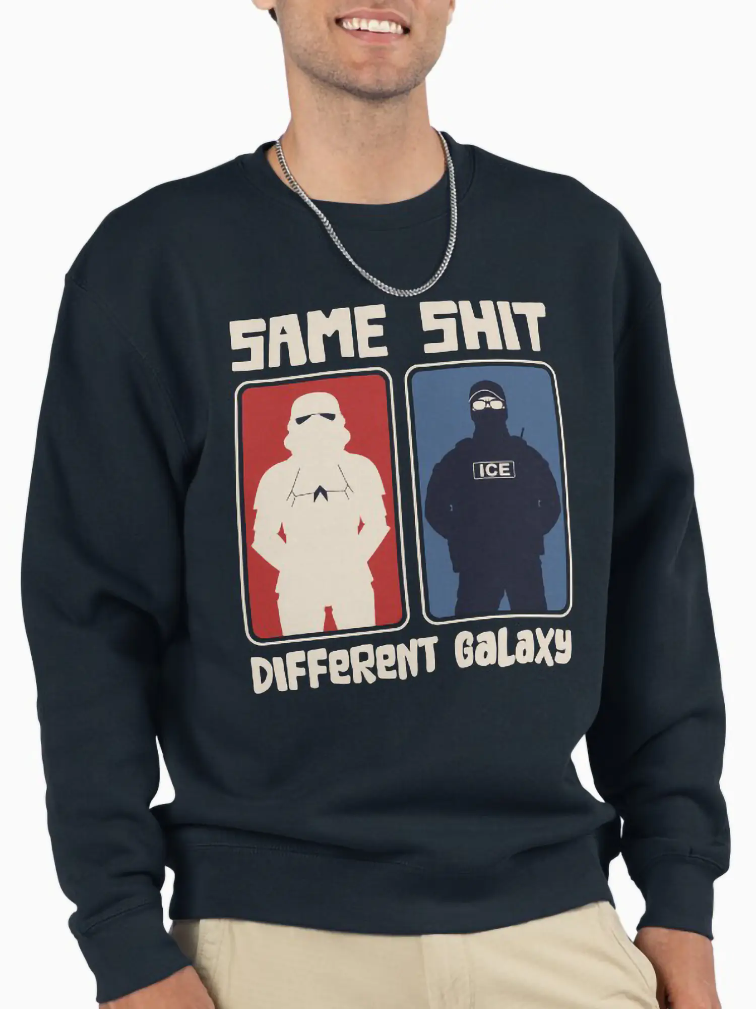 A man wearing a navy blue crewneck sweatshirt with a silver chain, displaying the 'Same Shit Different Galaxy' print as a bold statement of political fashion and anti-establishment sentiment.