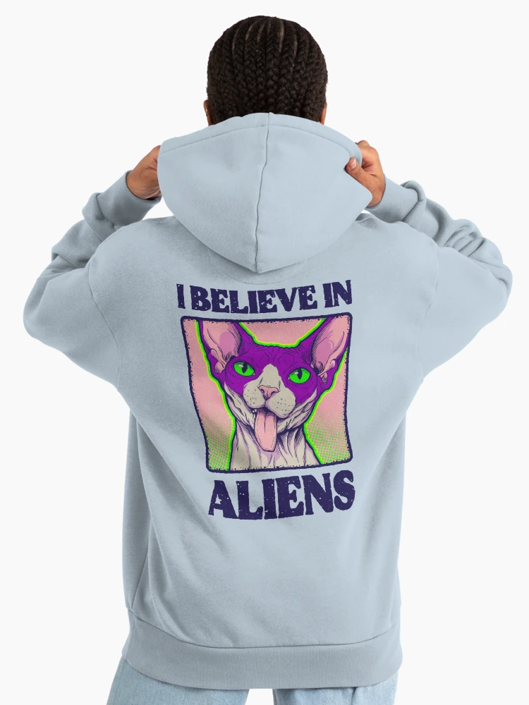 Woman wearing a light blue pullover hoodie with the 'I Believe in Aliens' feline spy graphic on the reverse.